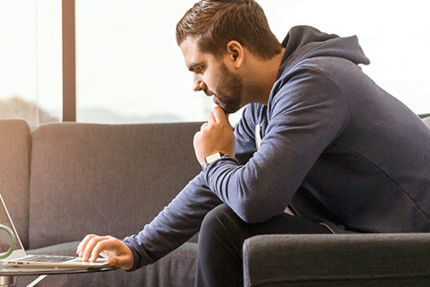 man i 25-årsåldern sitter i soffa framför laptop