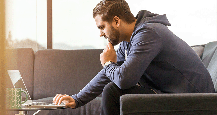 man i 25-årsåldern sitter i soffa framför laptop