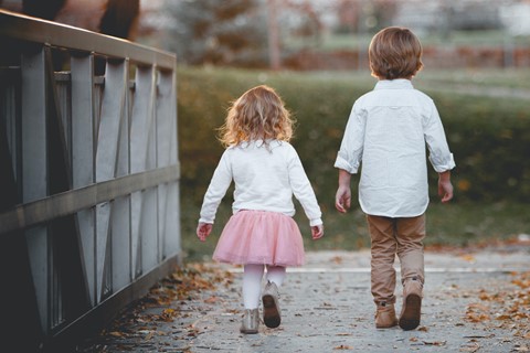 Två ljusklädda små barn syns bakifrån gående på en väg med höstlöv