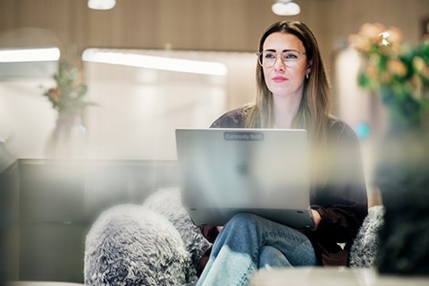 Kvinna sitter i soffa med laptop i knäet