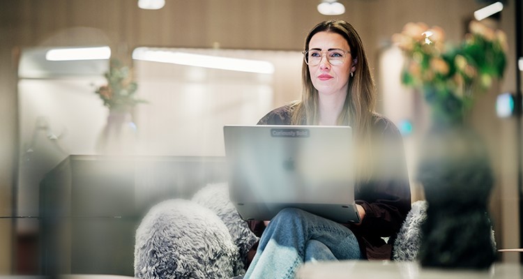 Kvinna sitter i soffa med laptop i knäet