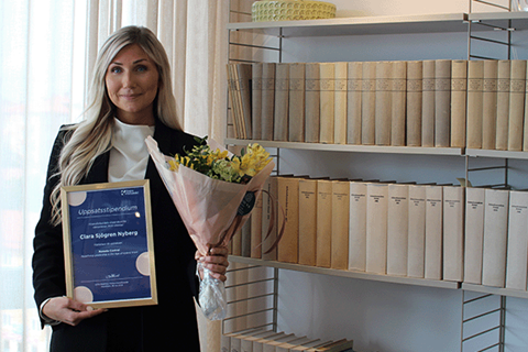 Ung kvinna står och håller diplom och blombukett framför en bokhylla