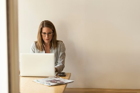 Kvinna sitter vid bord och kollar på laptop